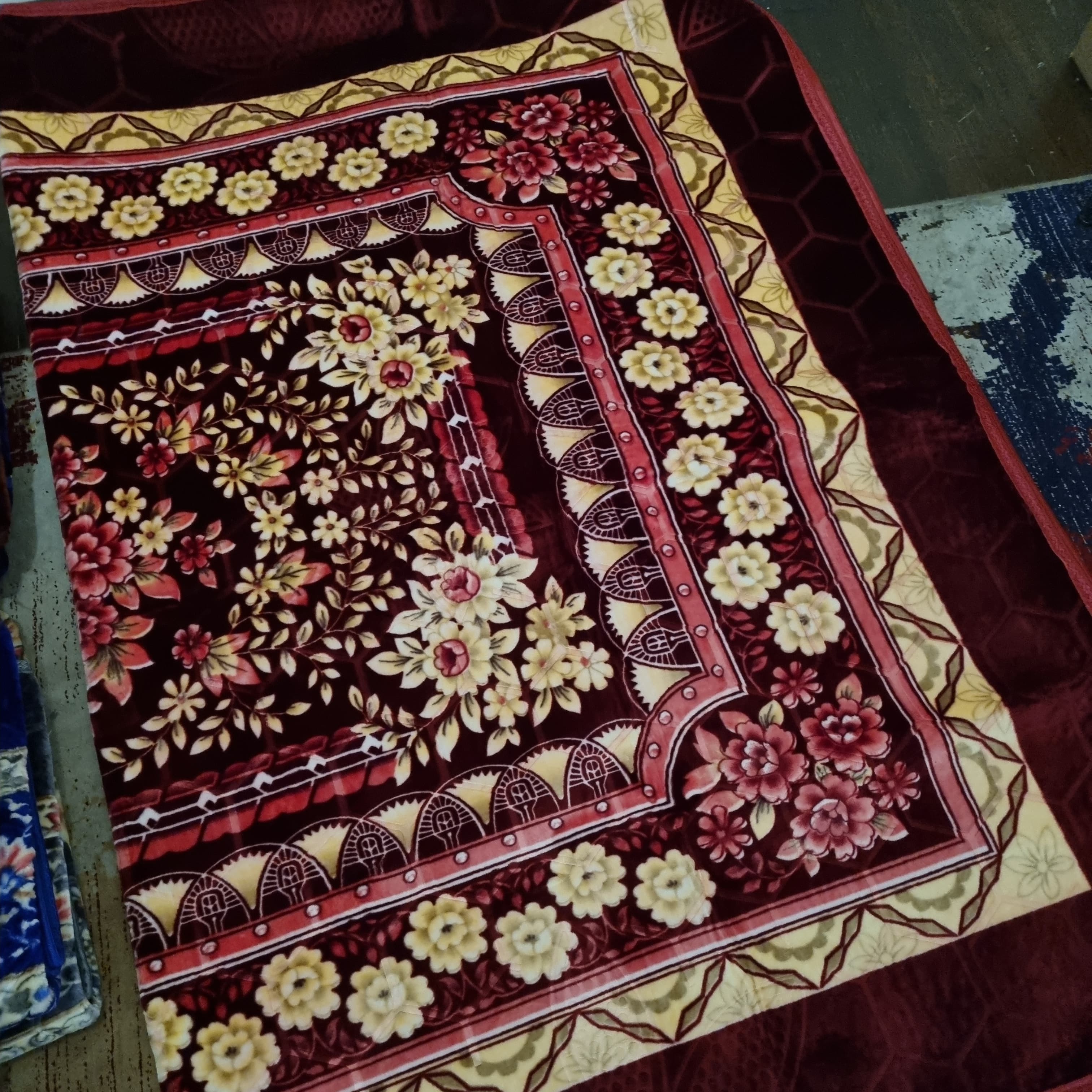A rectangular prayer mat with a floral pattern in cream, red, and brown colors.