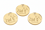 A gold-colored round tag with 'Eid Mubarak' written on it and a hanging lantern icon, against a white background